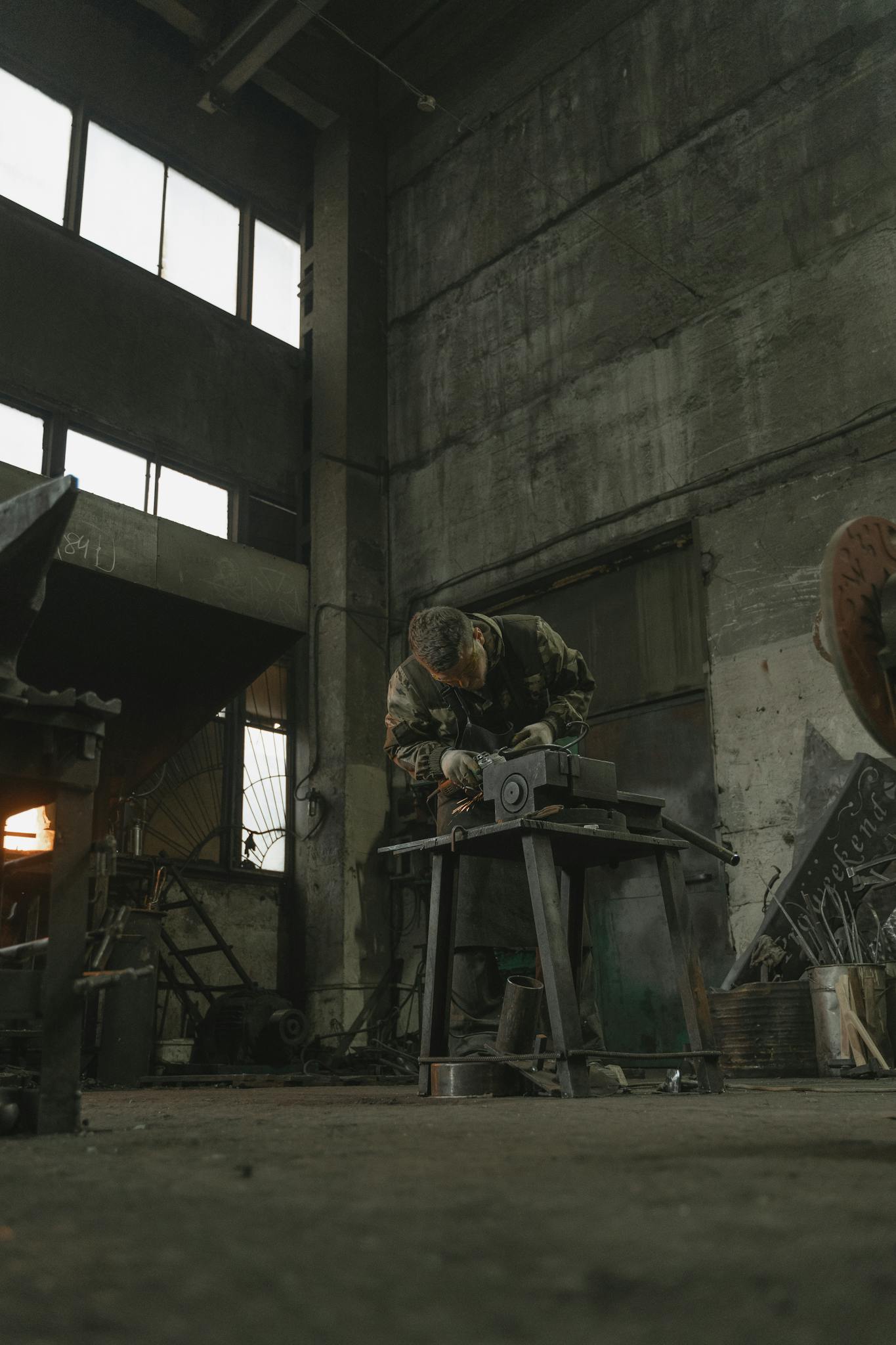 Metalworker in industrial setting using an angle grinder on metal piece, creating sparks.